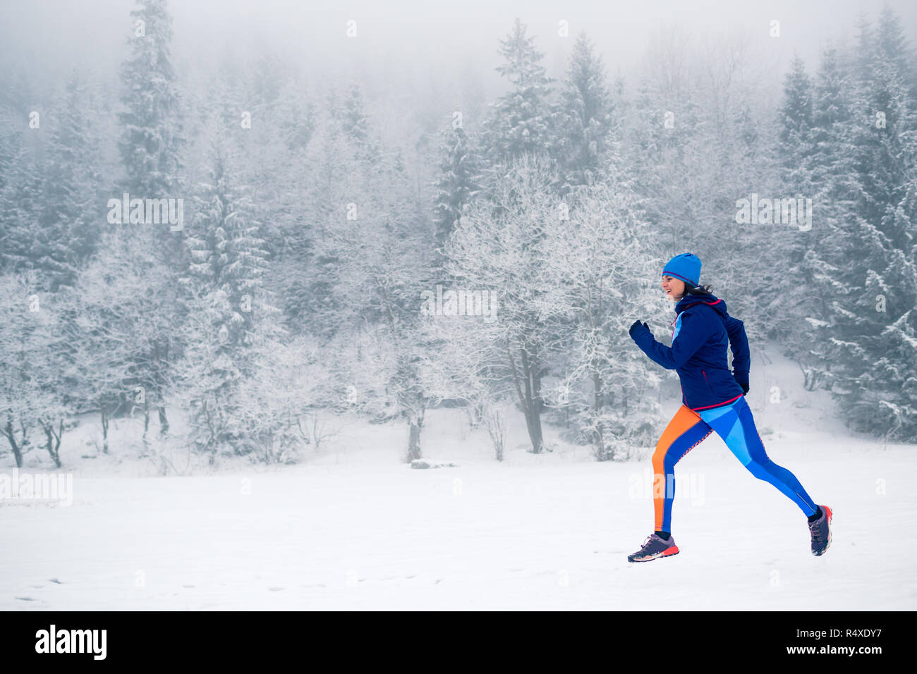 Woman trail running on snow in winter mountains and forest. Sport, fitness inspiration and motivation. Young happy girl athlete working out on snow Stock Photo