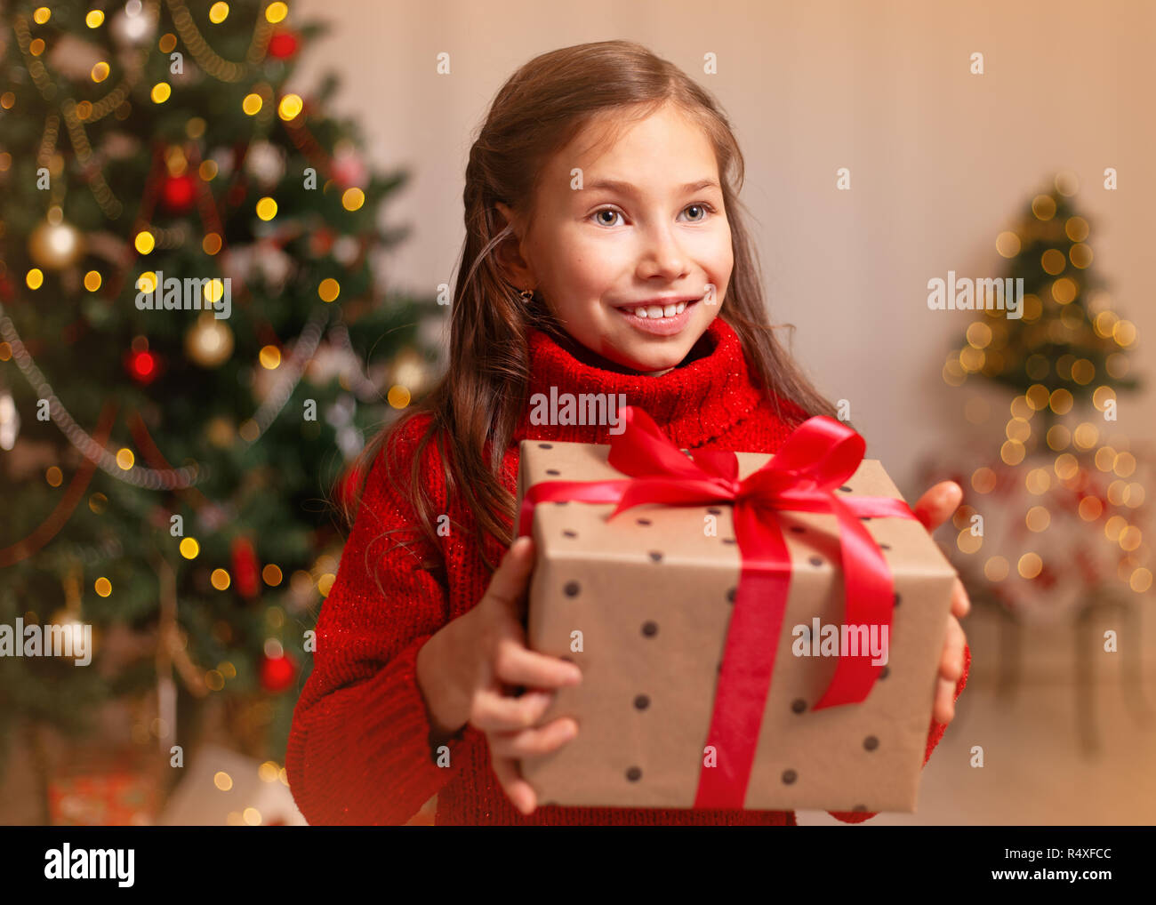 Cute little child girl with present gift box near Christmas tree at home. Stock Photo