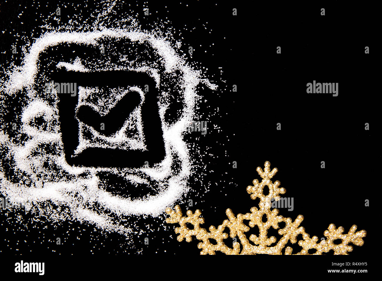 Checking mark symbol in checkbox drawing by finger on white salt powder spot cloud on left side on black background. Golden snowflake. New year and Christamas tick concept with place for text Stock Photo