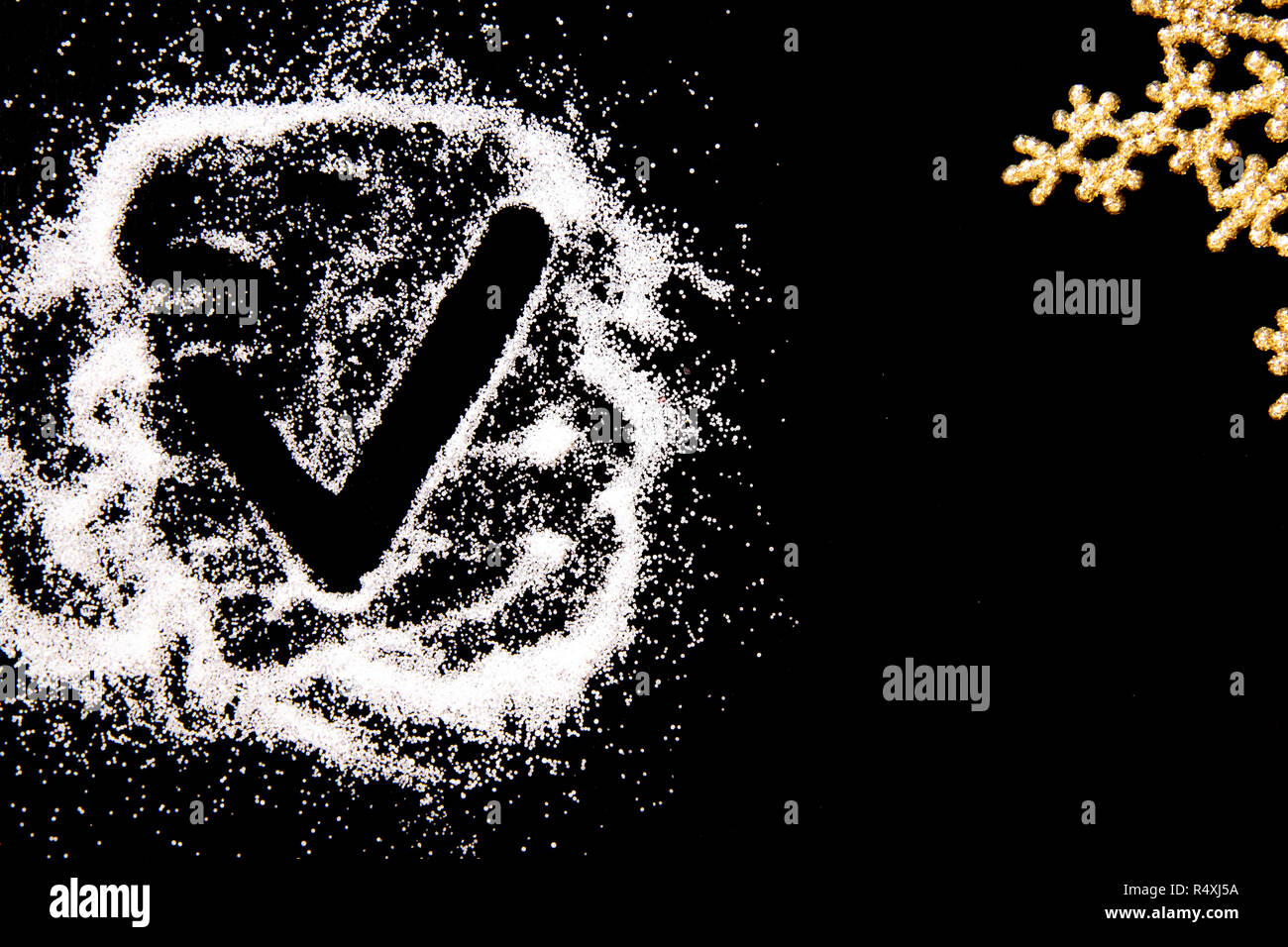 Checking mark symbol drawing by finger on white salt powder spot cloud on left side on black background. Golden snowflake in corner. New year and Christamas tick concept with place for text Copy space Stock Photo