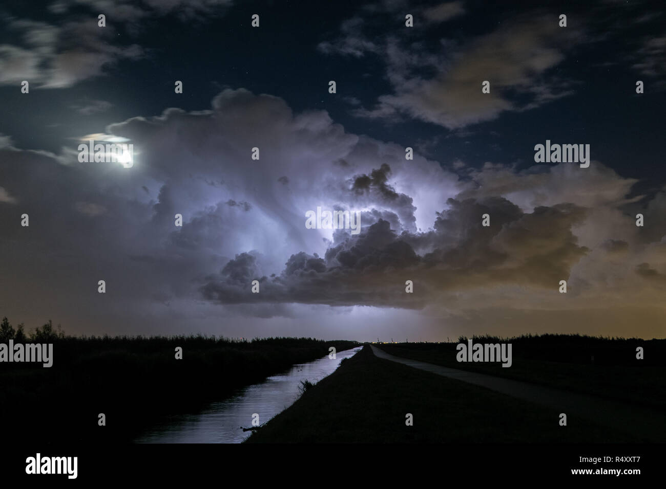 Thunderstorm clouds are illuminated by lightning. The moon is partly obscured by the storm. Location: close to the cities of Gouda and Leiden, Holland Stock Photo