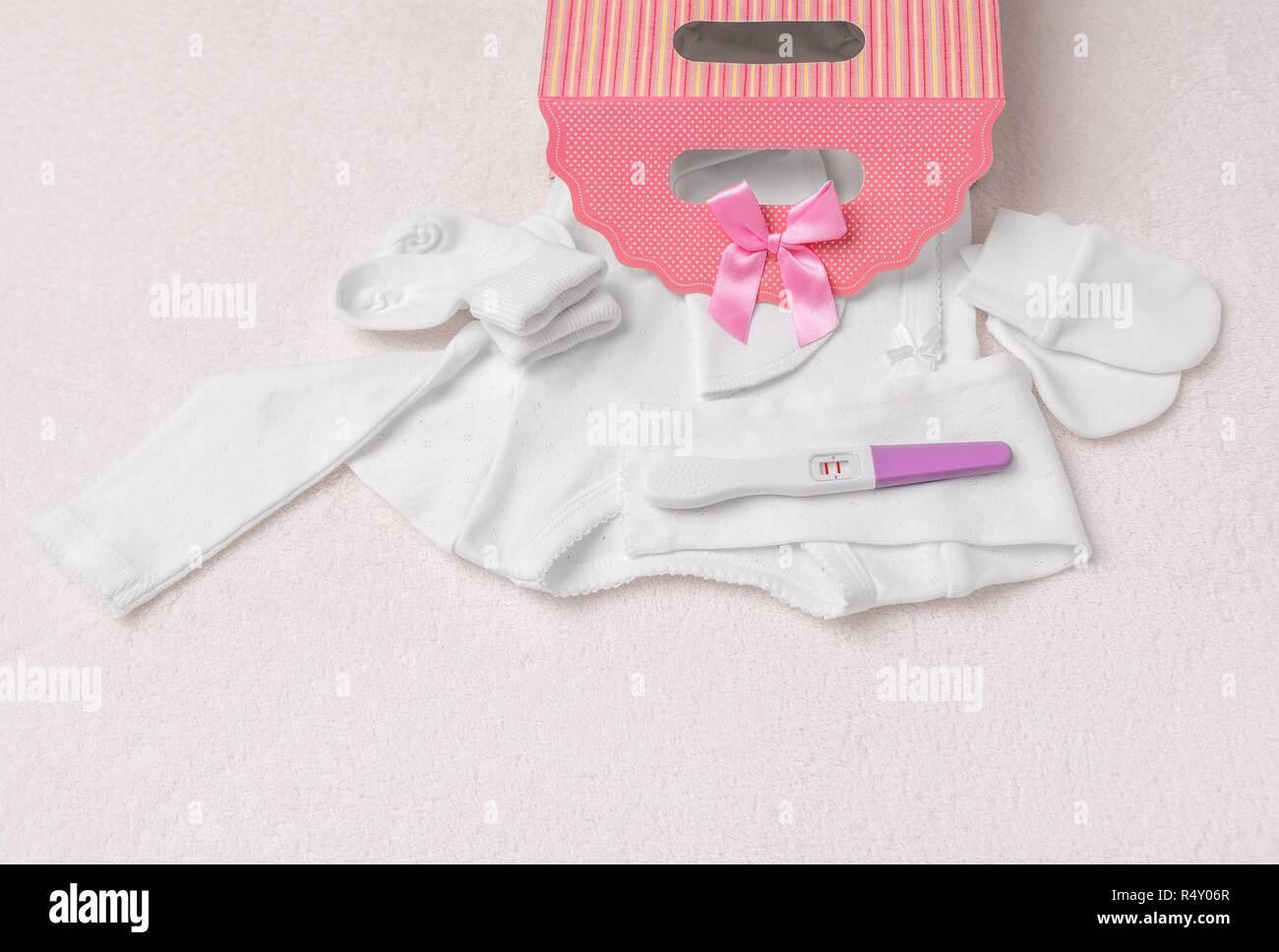 Pregnancy test and baby clothes. Beautiful still life on a plush blanket. Stock Photo