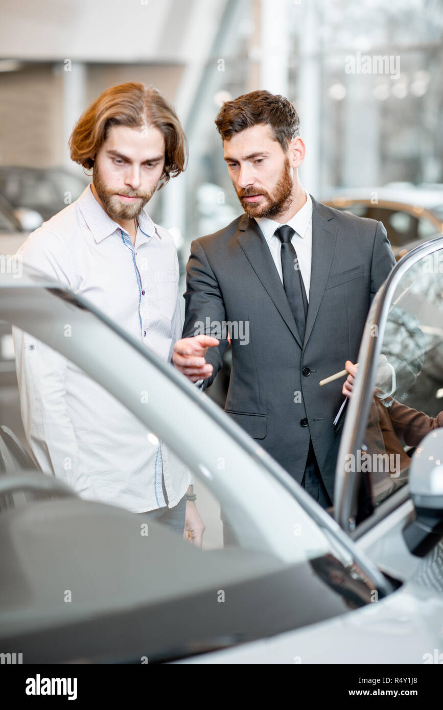 Car salesman helping a young male client to make a decision showing