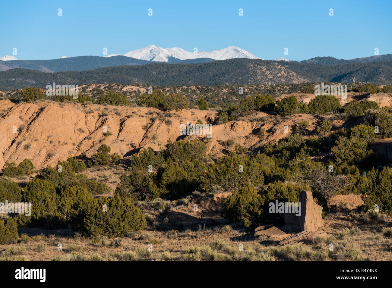 High desert red rock landscape contrasted with the snow-capped peaks of the Sangre de Cristo mountain range in the distance near Santa Fe, New Mexico Stock Photo