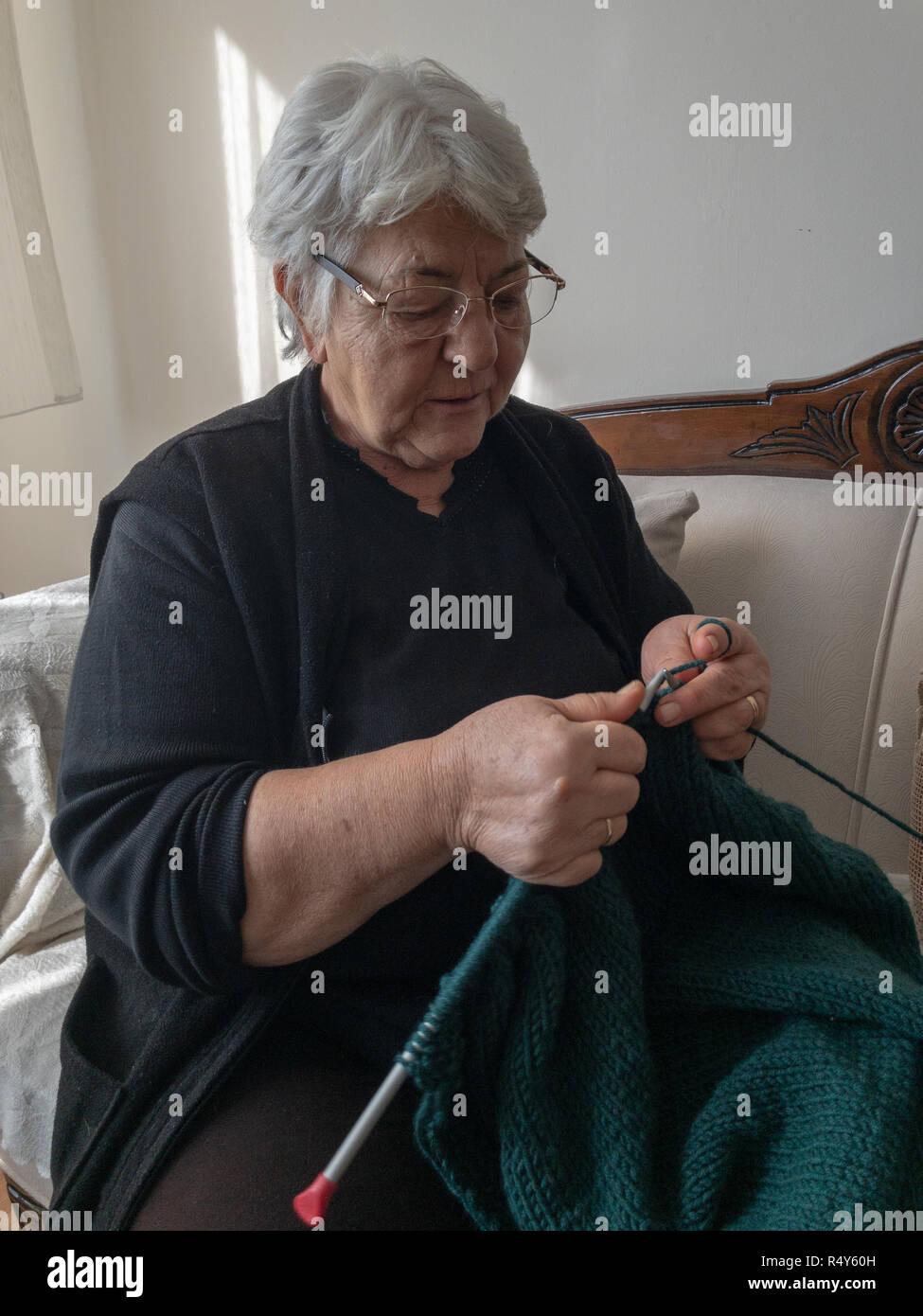 Old woman knitting while sitting sofa Stock Photo Alamy
