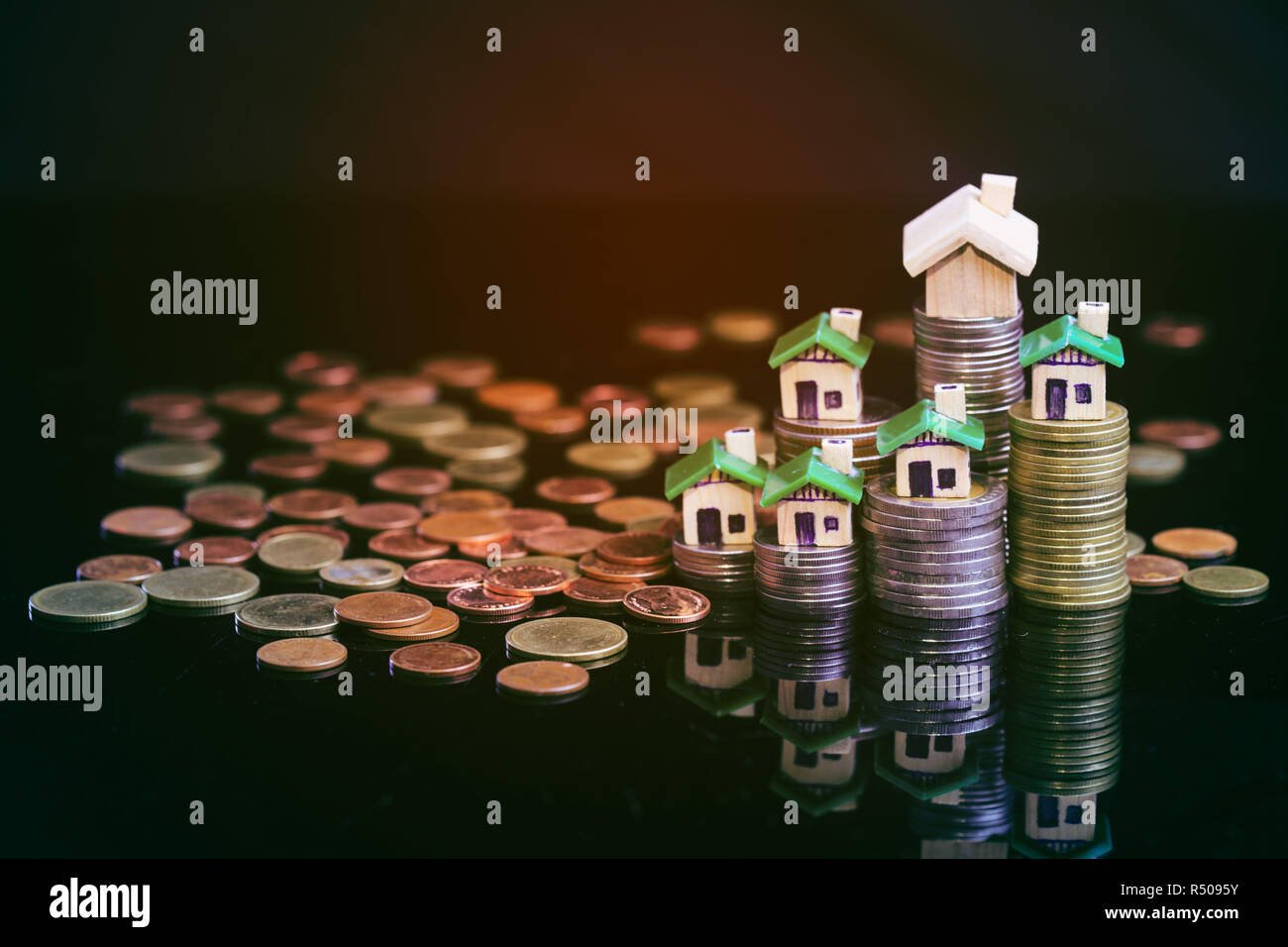 image for property investment. Creatively lit green house and stacked coins against a black background. concept mortgage and real estate investment. Stock Photo