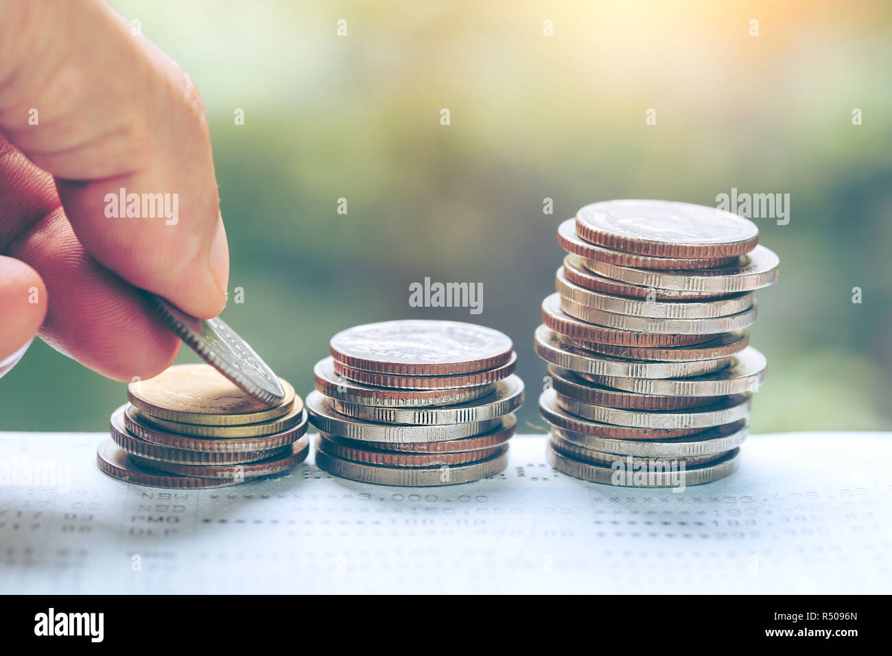 business and money saving concept - close up of man hand putting euro coins into columns, coins stack in front of bank account book Savings money of c Stock Photo