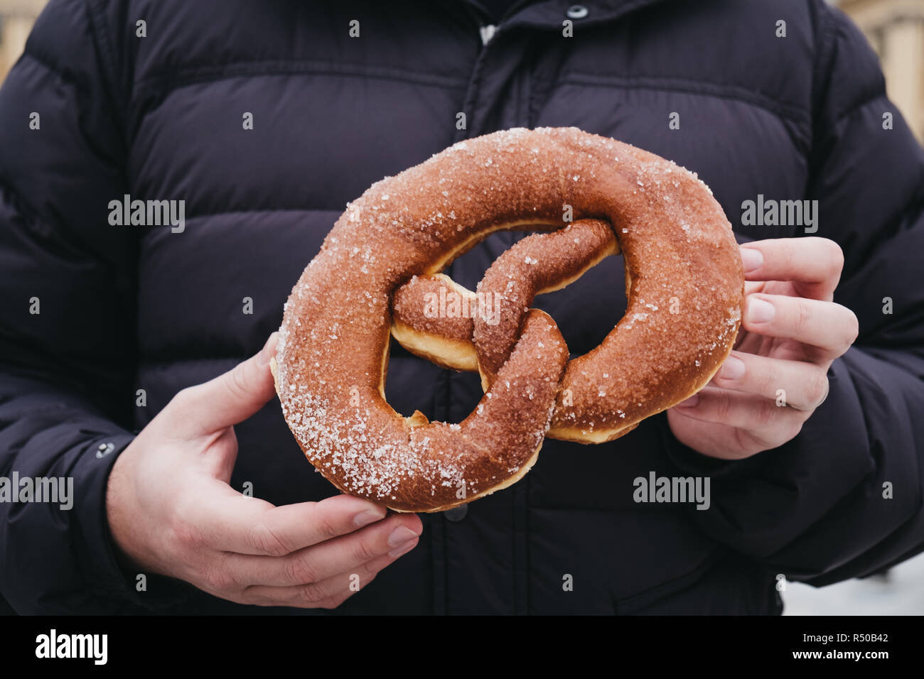 Unidentified person wearing winter jacket holding freshly made donuts pretzel in hands. Stock Photo