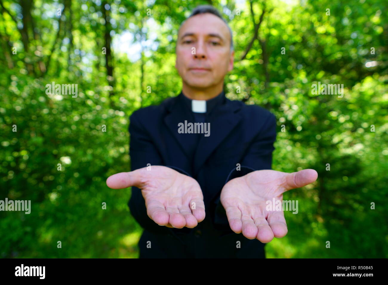 A good looking catholic priest is welcoming us in joy. He looks at us with confidence, openning his arms in peace. Focus on hands. Stock Photo
