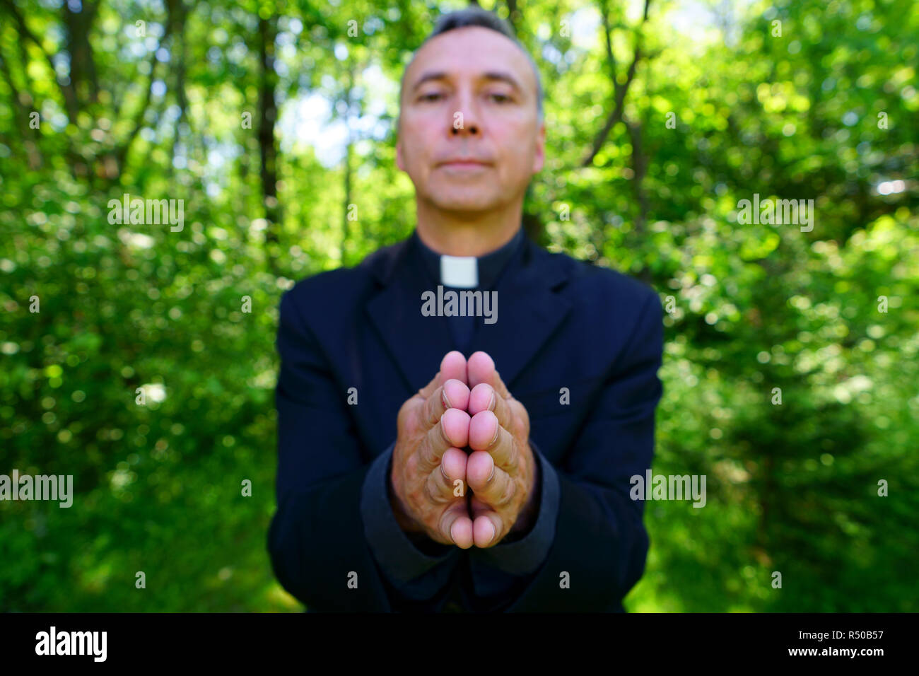 A good looking catholic priest is praying with us in joy. He looks at us with confidence, openning his arms in peace. Focus on hands. Stock Photo