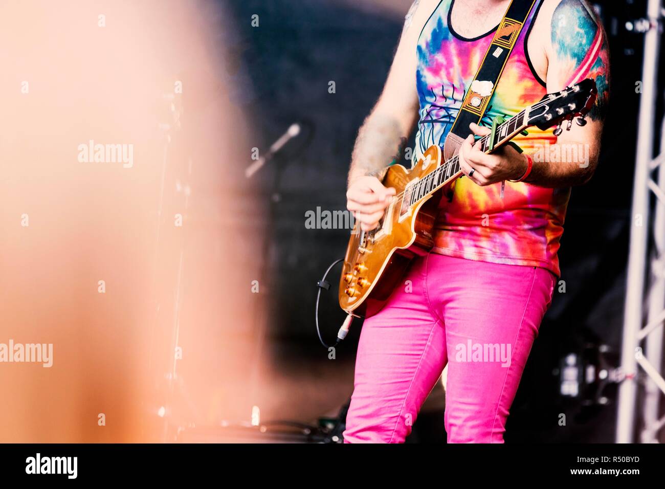 Lead guitarist in a rock or heavy metal band in a tie dyed vest playing electric guitar on stage at a festival in the UK Stock Photo
