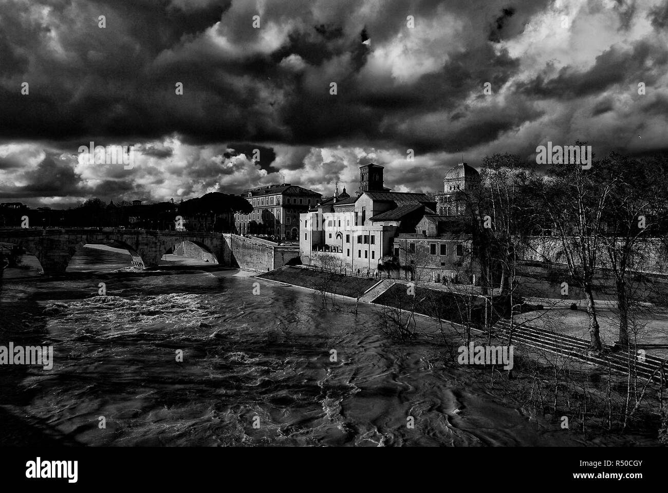 Winter in Rome. River is swollen along Tiber Island embankments under stormy clouds (Black and White) Stock Photo
