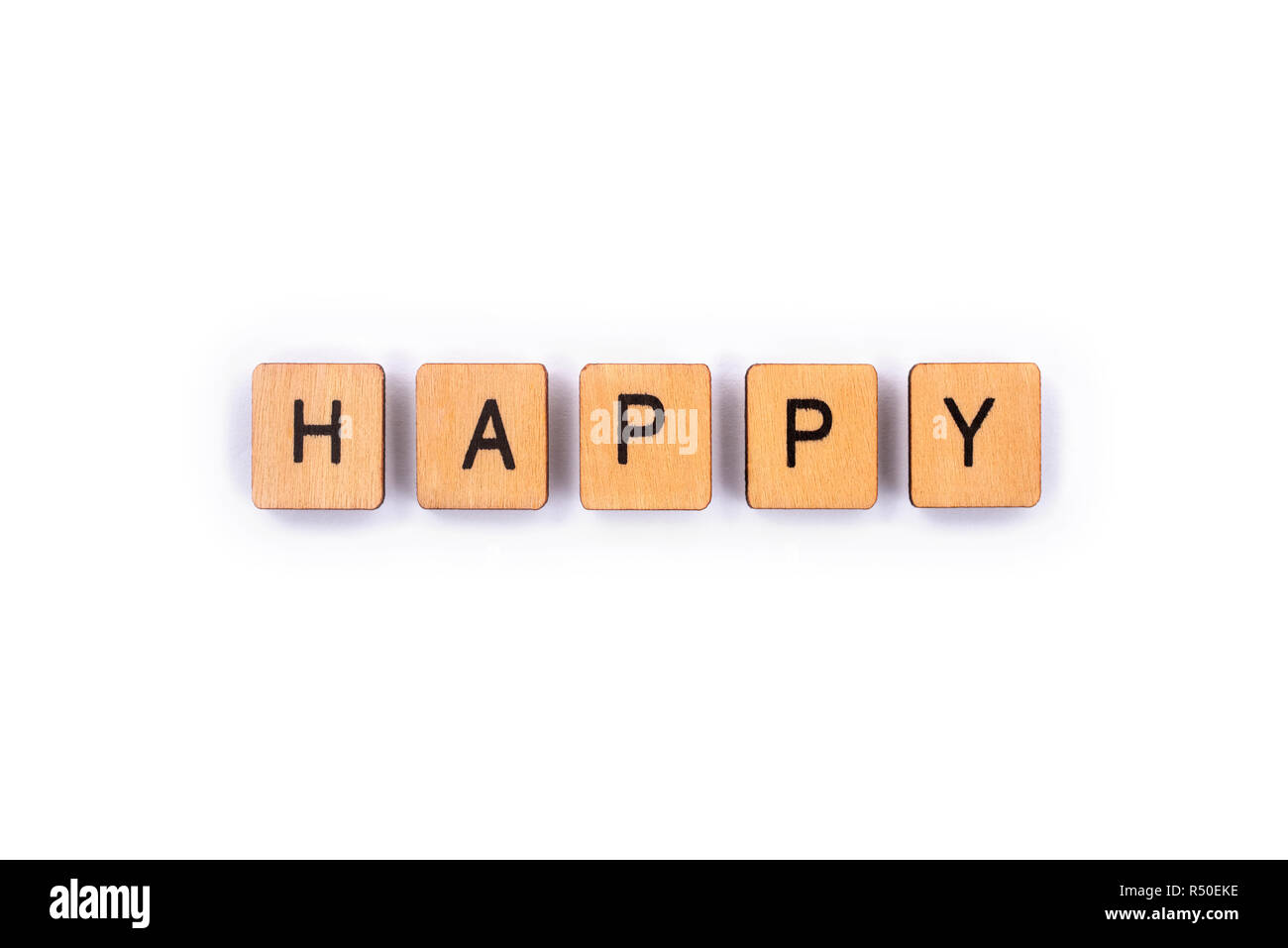 HAPPY, spelt with wooden letter tiles over a plain white background. Stock Photo