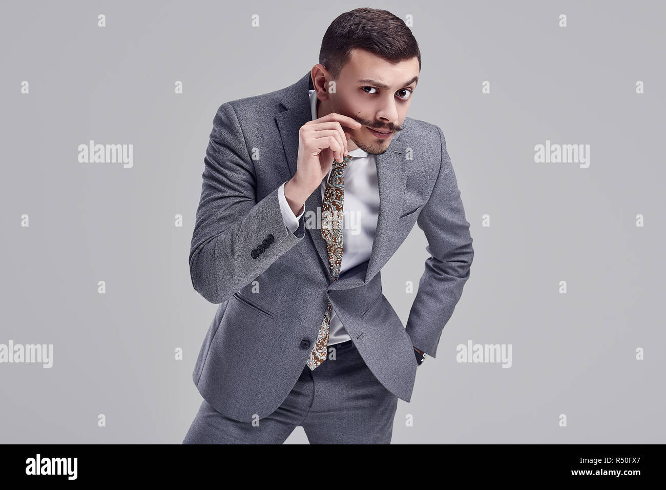 Portrait of handsome young confident arabic businessman with fancy mustache in fashion gray full suit on studio background Stock Photo