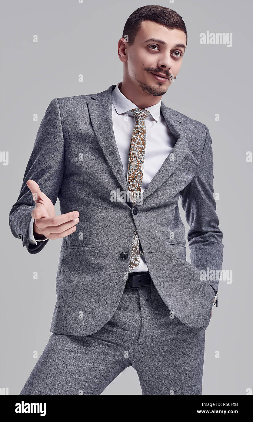 Portrait of handsome young confident arabic businessman with fancy mustache in fashion gray full suit on studio background Stock Photo