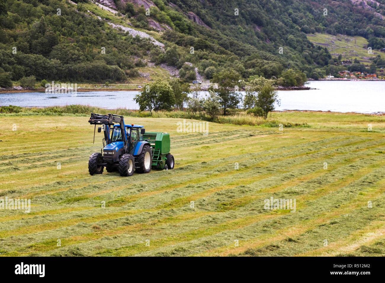 Small tractor with round baler haymaking on a field in Geiranger, Norway. Stock Photo