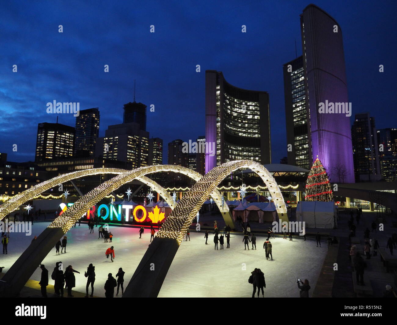 Skating rink with Christmas lights and lit Toronto sign, evening in front of Toronto's modern City Hall Stock Photo