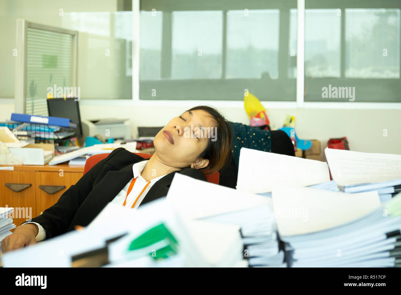 Exhausted Businesswoman Sleeping On Desk In Office With Pile Of