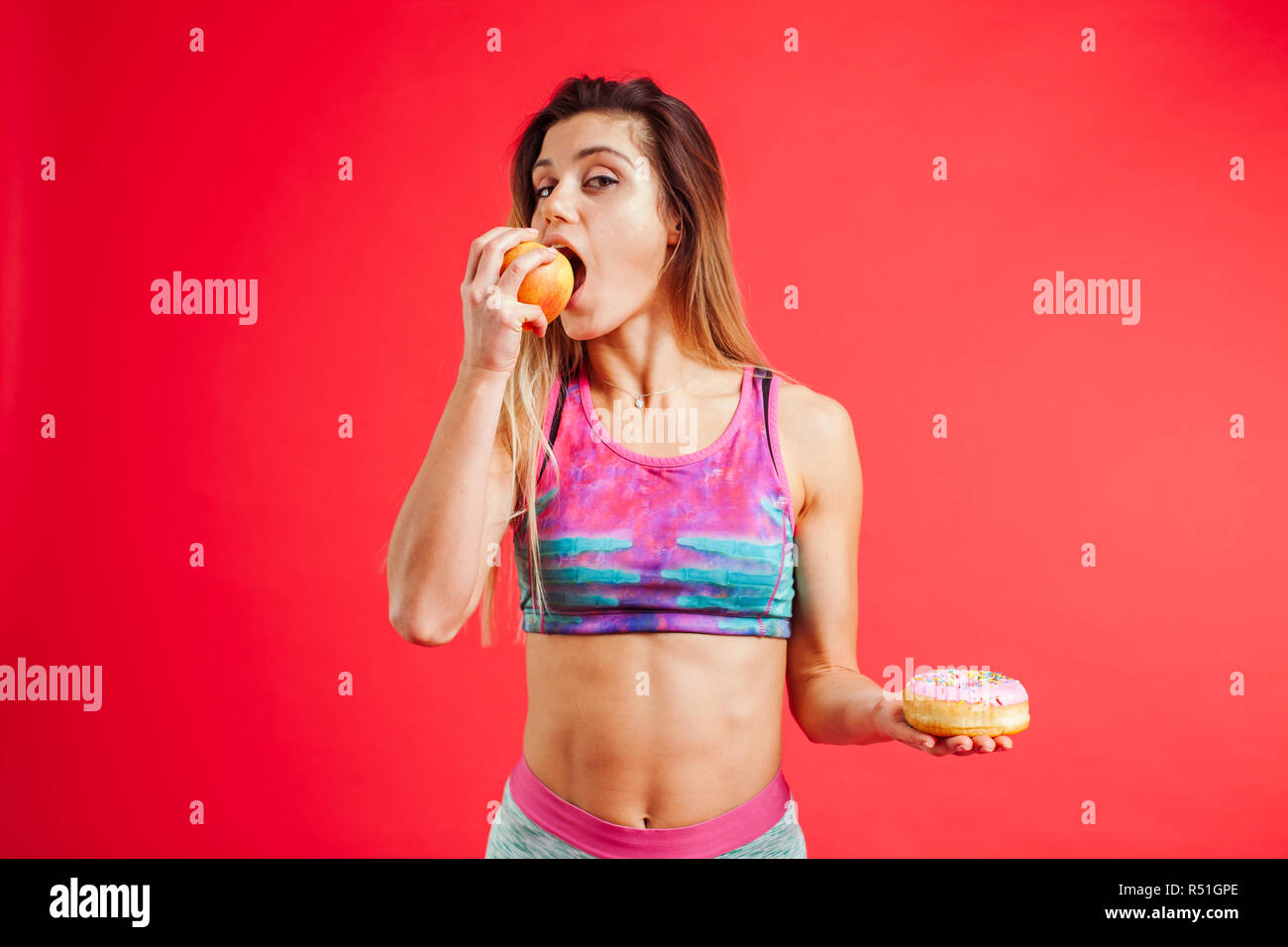 Portrait of a young woman choosing between  appel and a donut isolated over white background Stock Photo