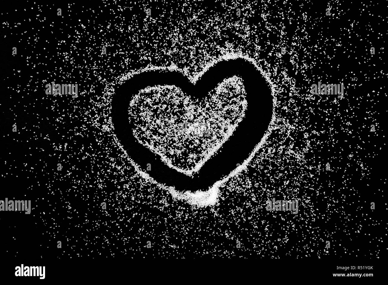 Closed love heart symbol drawing by finger on white salt powder on black background. Romantic St. Valentines Day holidays concept with place for text. Copy space. Stock Photo