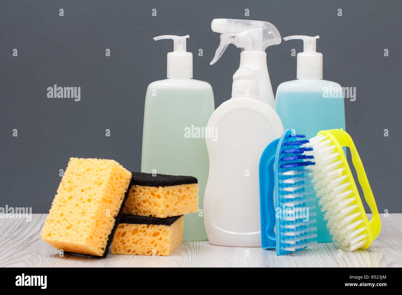 Plastic bottles of dishwashing liquid, glass and tile cleaner, detergent for microwave ovens and stoves, brushe and sponge on gray background. Stock Photo