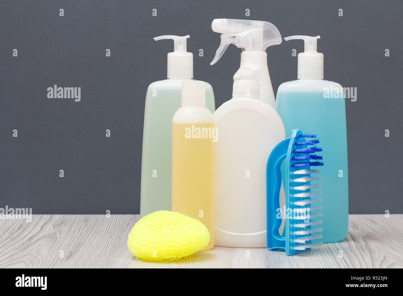 Plastic bottles of dishwashing liquid, glass and tile cleaner, detergent for microwave ovens and stoves, brushe and sponge on gray background. Stock Photo