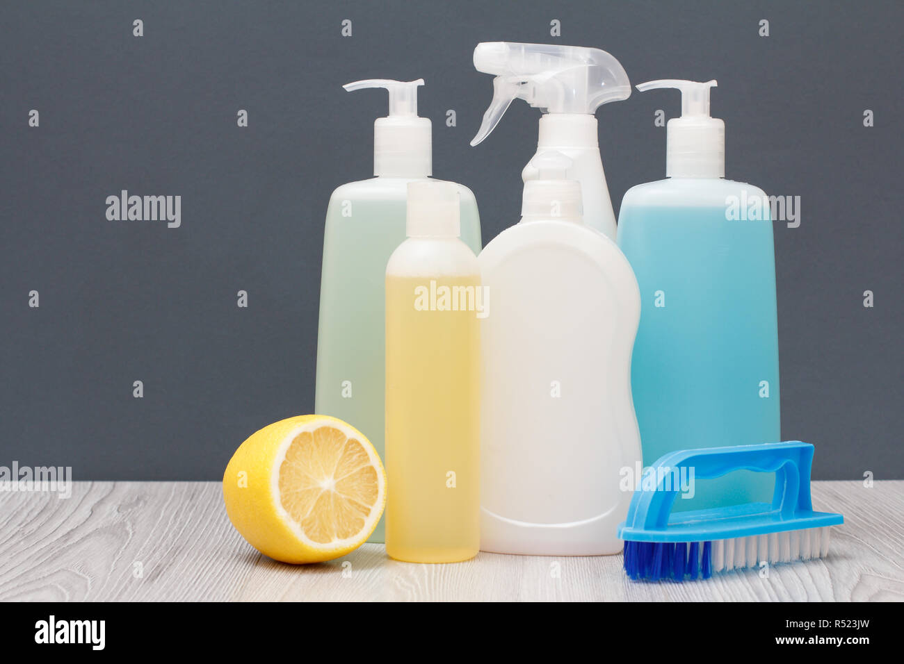 Plastic bottles of dishwashing liquid, glass and tile cleaner, detergent for microwave ovens and stoves, brushe and lemon on gray background. Stock Photo