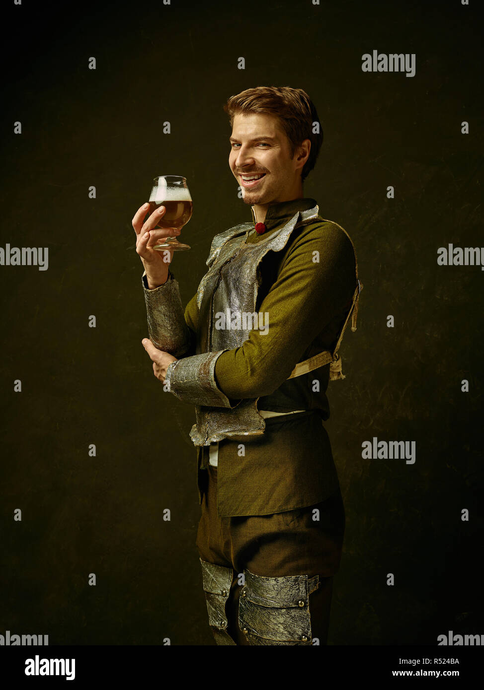 Medieval smiling happy knight with beer on dark studio background. Portrait in low key of brutal man in tradishional retro costume of spanish hidalgo. Human emotions, comparison of eras concept Stock Photo