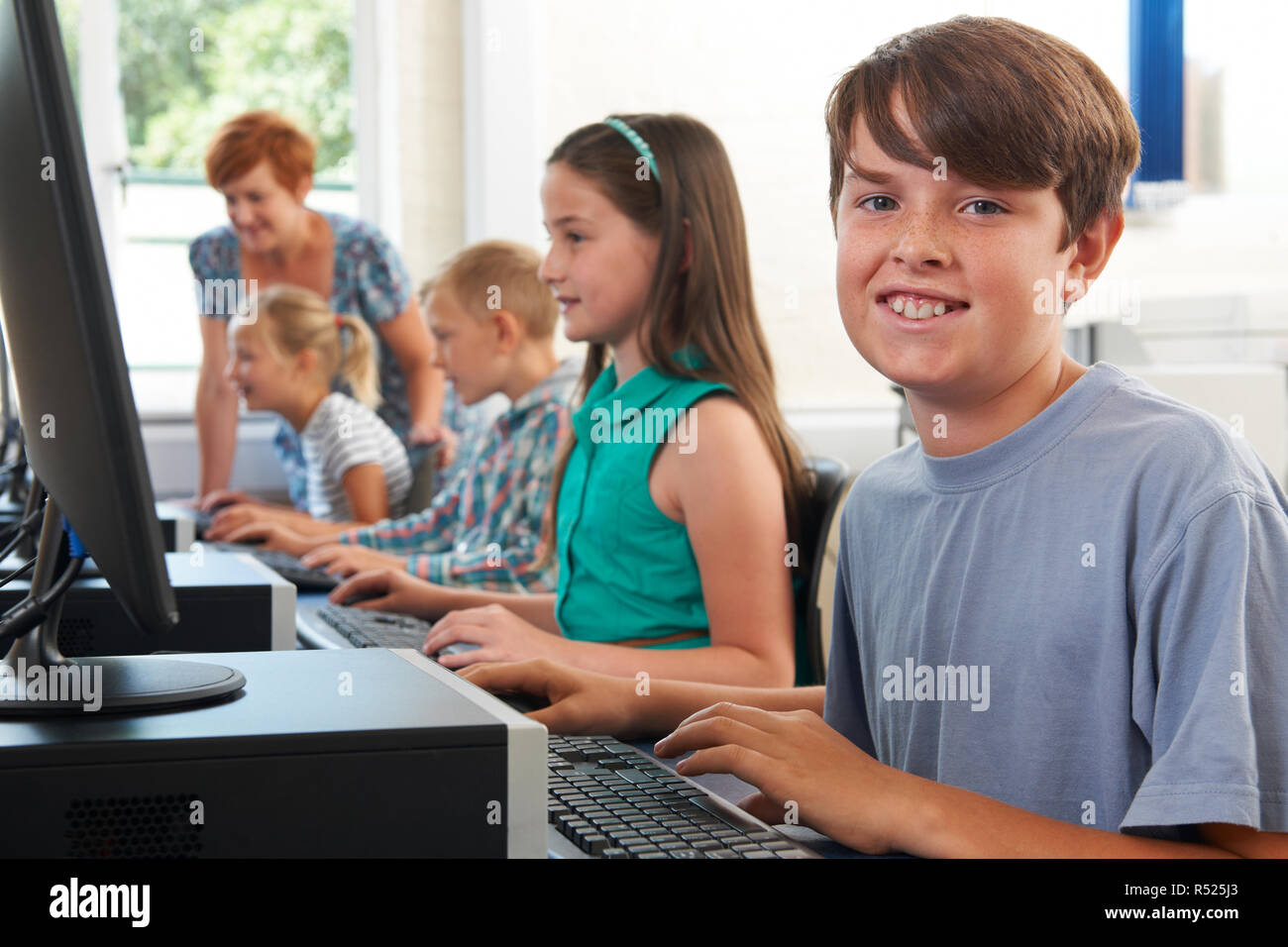 Portrait Of Male Elementary Pupil In Computer Class With Teacher Stock Photo