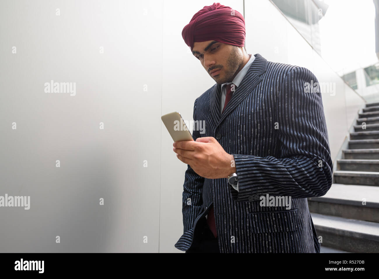Portrait of Indian businessman with turban outdoors in city using phone Stock Photo