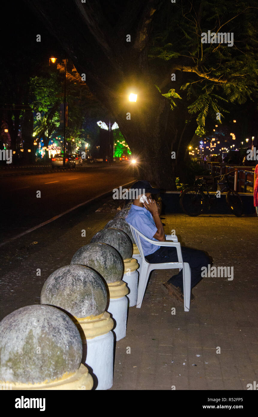 An on duty security guard sits and talks on phone at the 49th International Film Festival of India in Panaji, Goa, India. Stock Photo