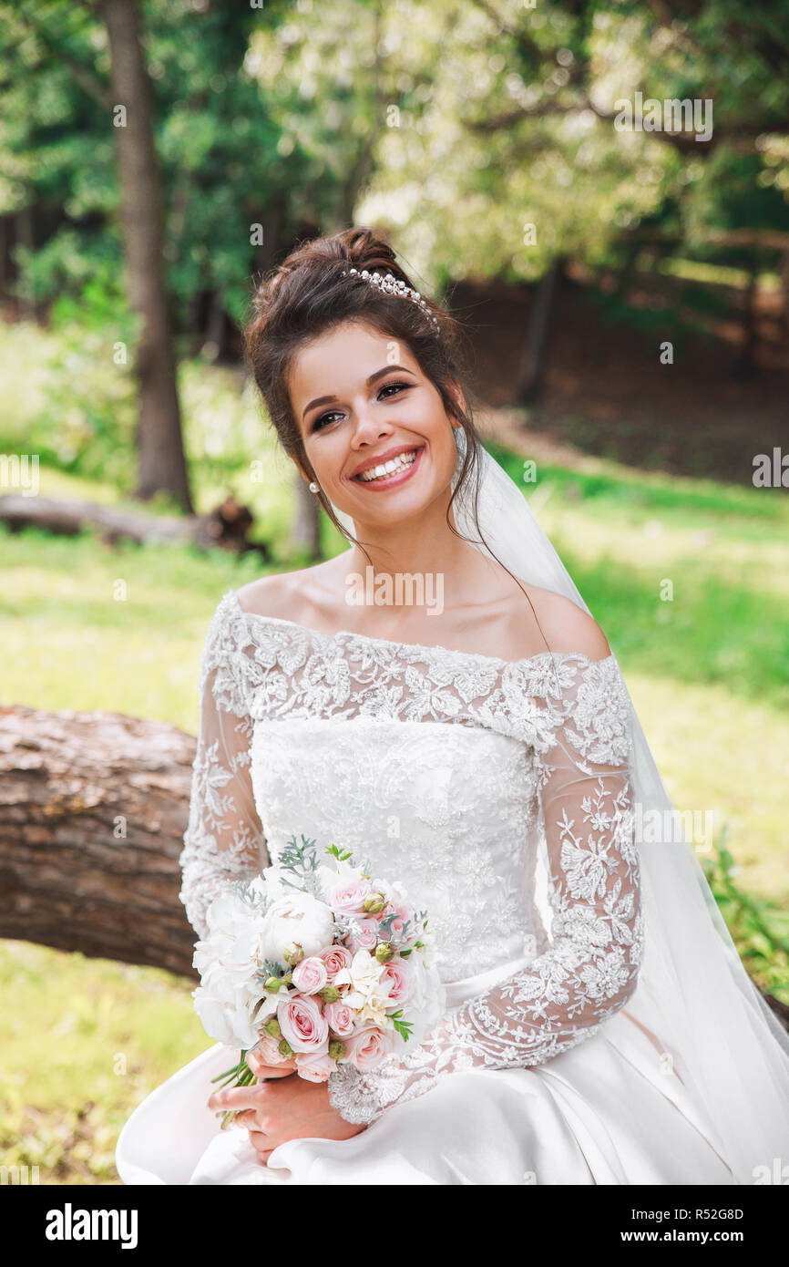Beautiful happy bride with bouquet of flowers in park Stock Photo - Alamy