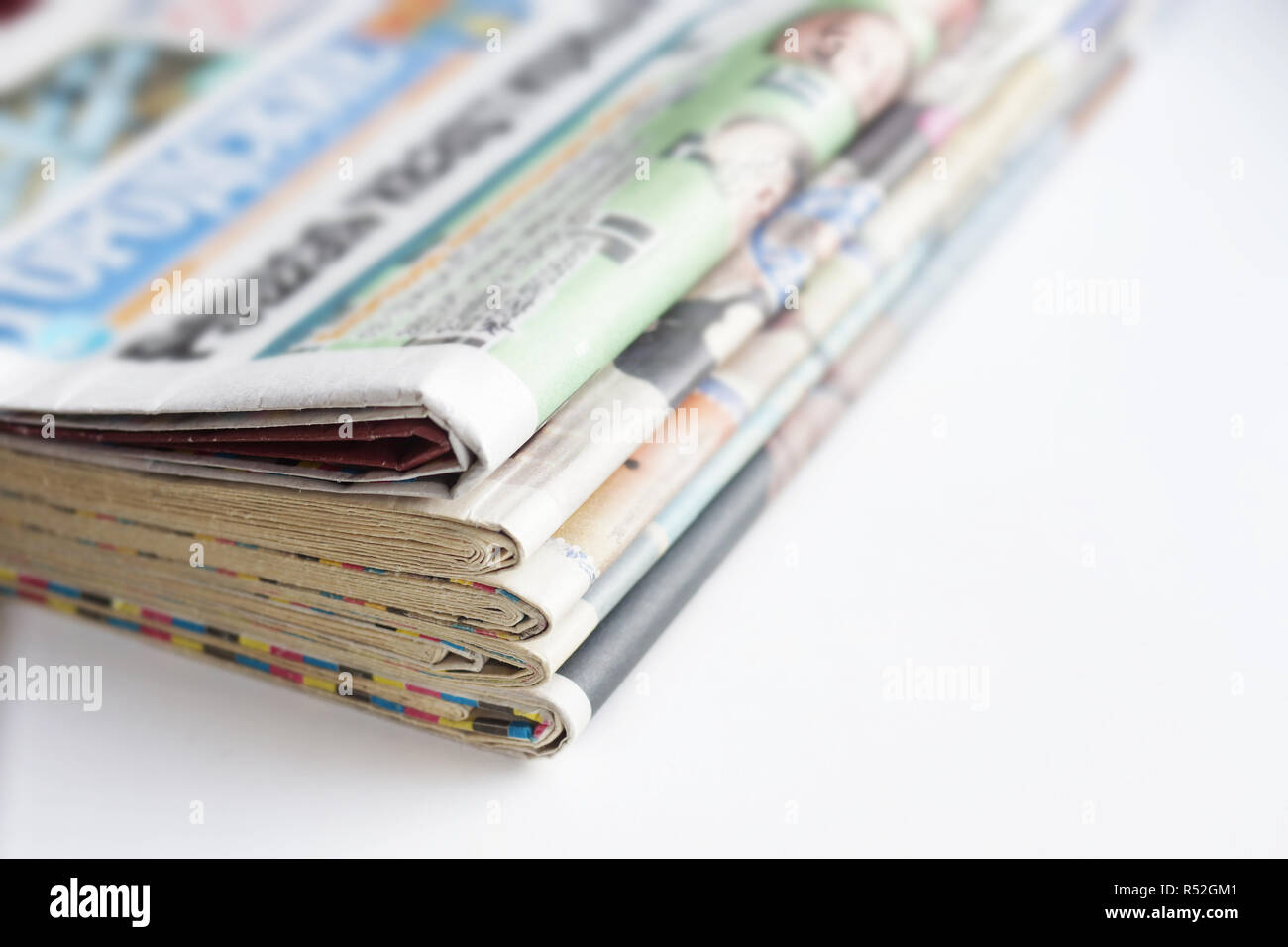 Stack of newspapers and magazines with colorful pages (headlines, articles), latest news in daily papers. Tabloid journals stacked in pile on white Stock Photo