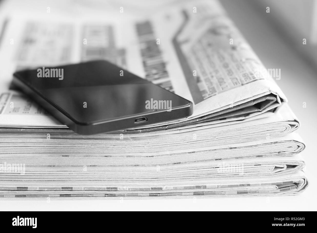 Newspaper and smartphone. Tabloid journals and cell phone - business concept. News magazines folded and stacked in pile and mobile gadget on the stack Stock Photo