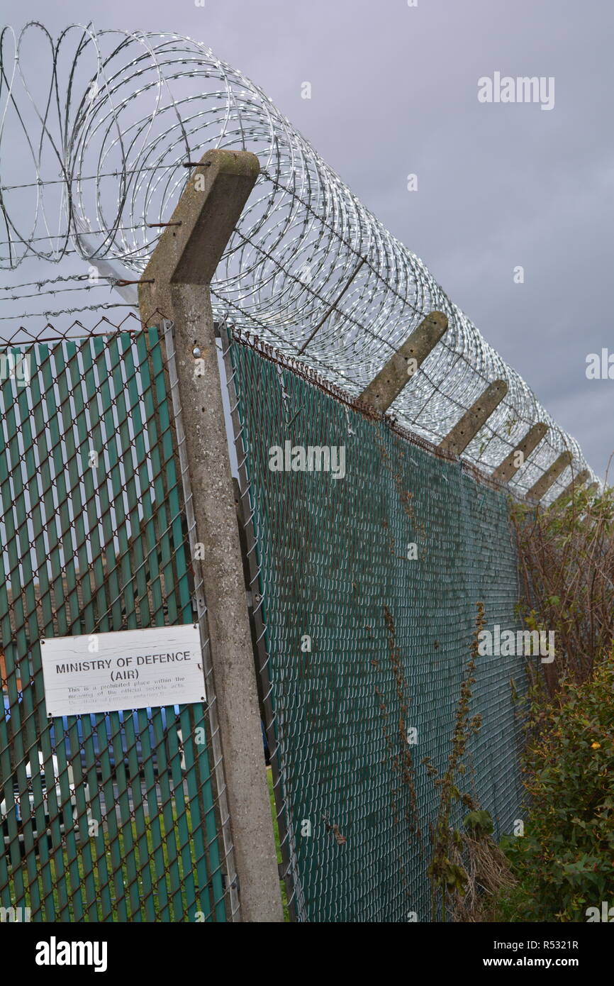 Rolled razor wire glinting against a dark sky atop the fence of an AMERICAN airforce base Stock Photo