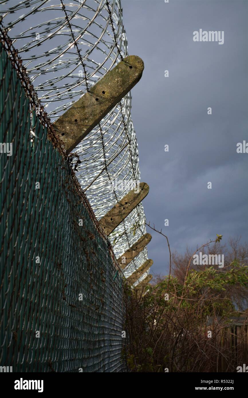 Rolled razor wire glinting against a dark sky atop the fence of an AMERICAN airforce base Stock Photo
