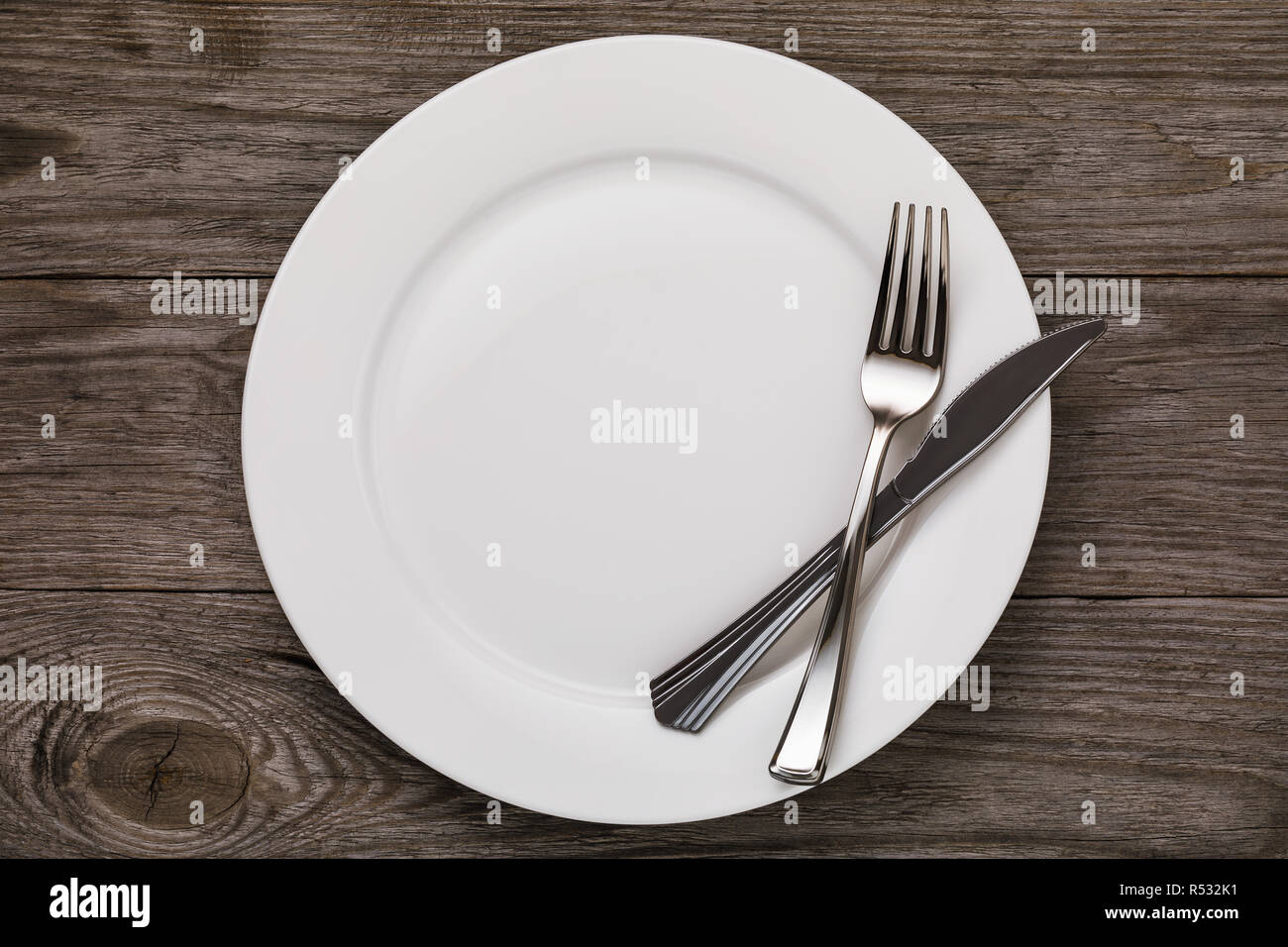 Empty white ceramic plate and cutlery on wooden table, top view Stock Photo