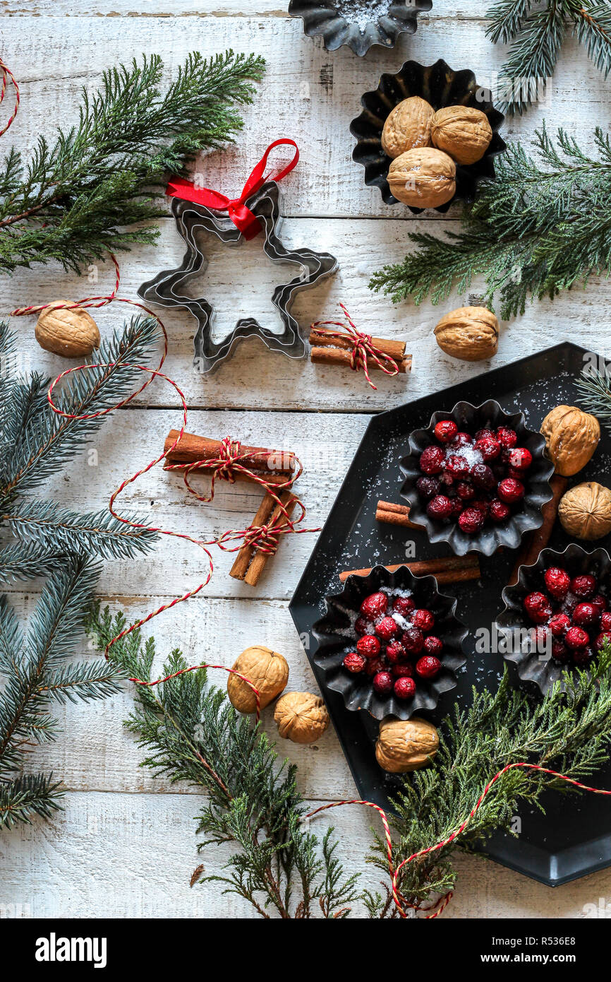Festive table with red berries, nuts, cinnamon sticks and evergreens on a white wooden background Stock Photo
