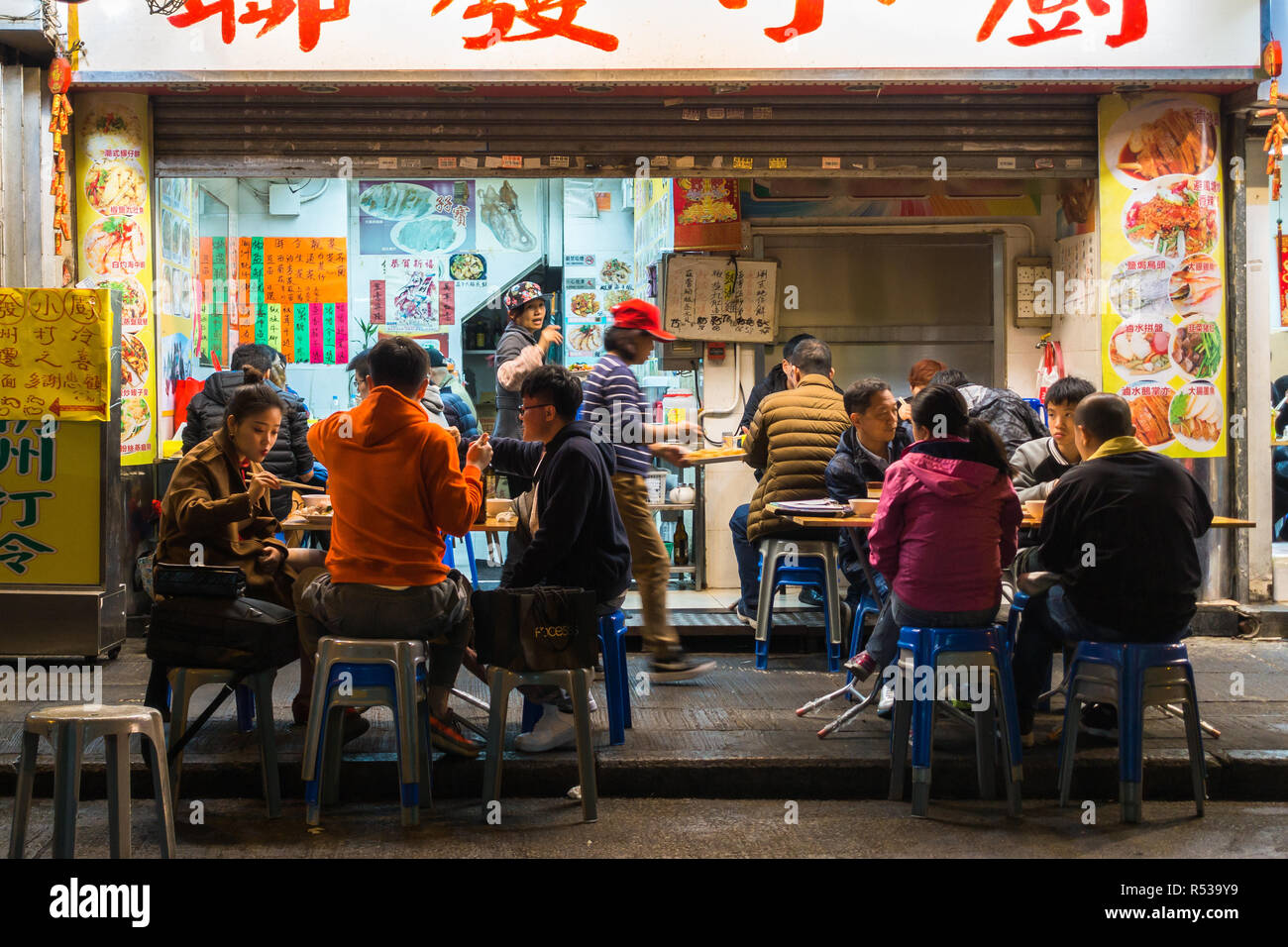 Street scene with local people dine at a street vendor in Mong Kok area. Hong Kong, Kowloon, January 2018 Stock Photo