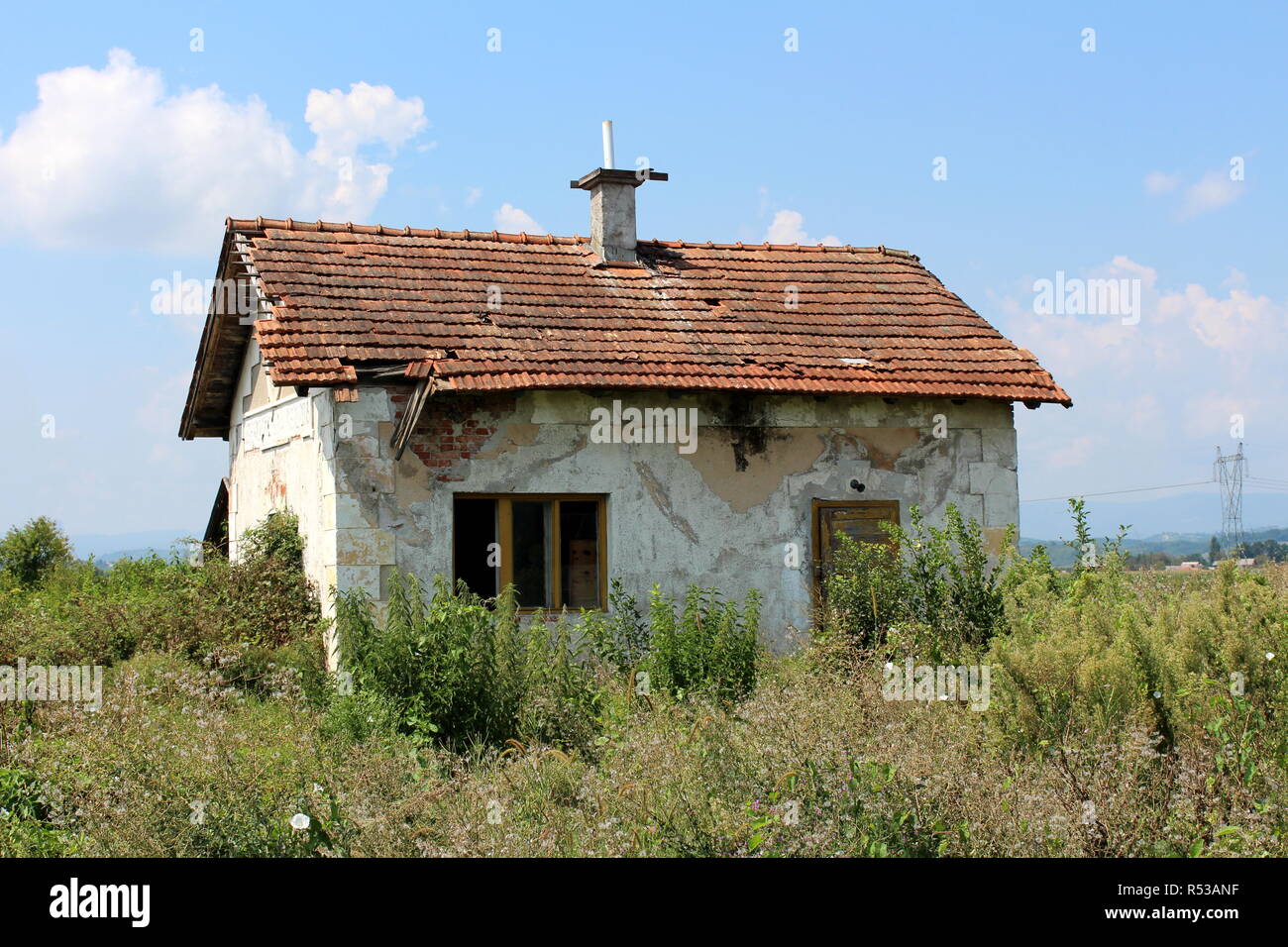 Small abandoned red bricks house with dilapidated white facade, destroyed  roof tiles, doors and windows completely surrounded with high grass Stock  Photo - Alamy