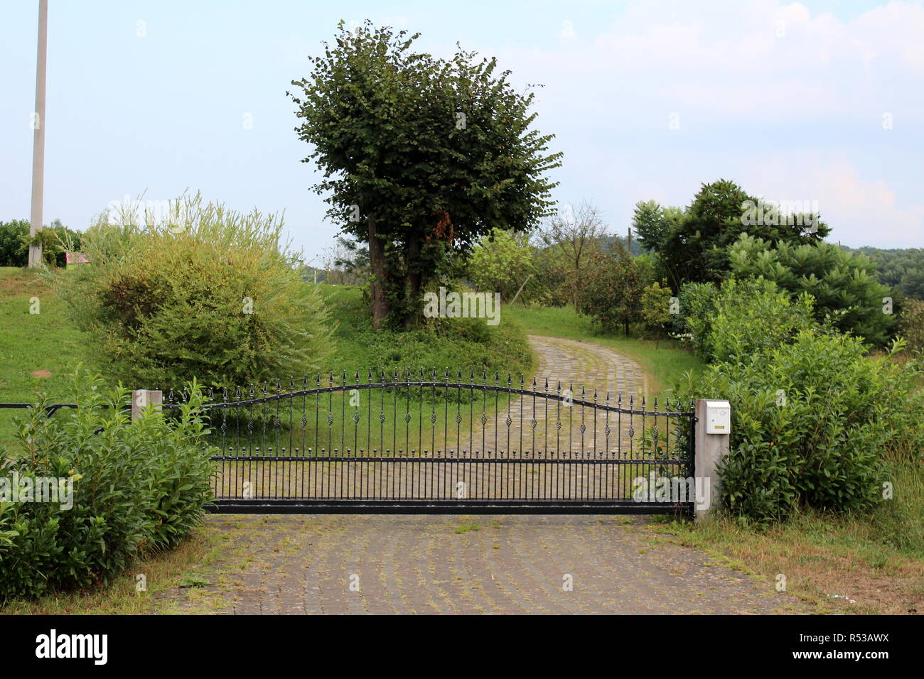 Stone tiles driveway leading to black wrought iron gate mounted on two