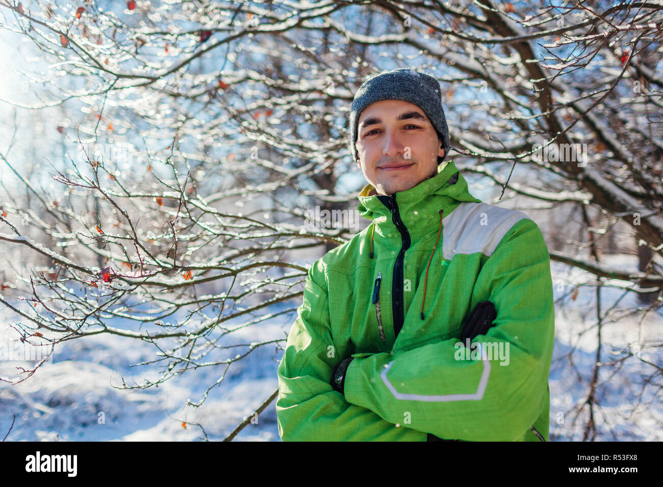 Young man wearing sportive clothes in winter forest. Smiling guy looking at camera with hands crossed Stock Photo