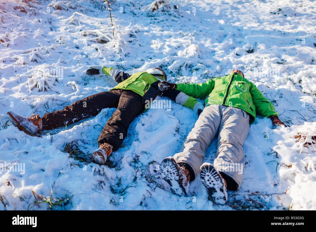 Young couple in love lying in snow and making snow angels. Happy people having fun in winter forest. Seasonal activities Stock Photo