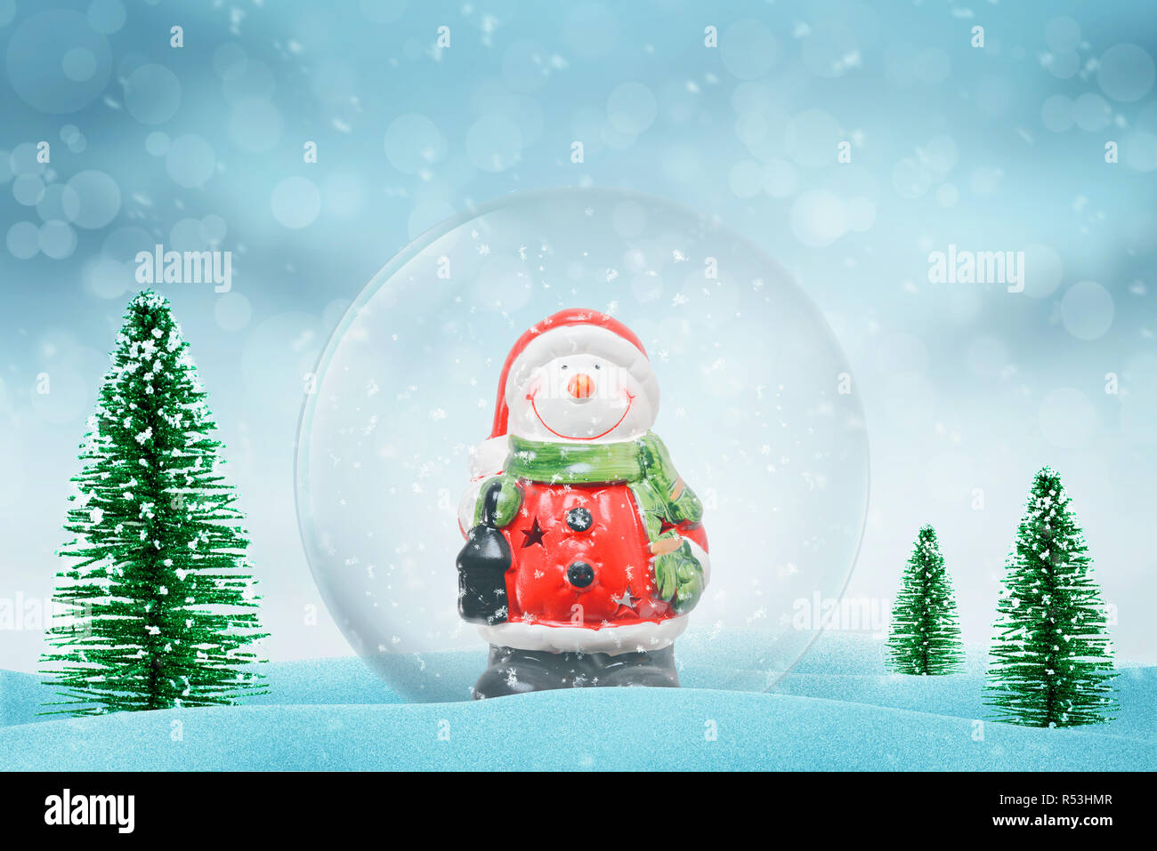 Christmas magic snow ball with Snowman. Snow falls in background. Christmas trees beside. Stock Photo
