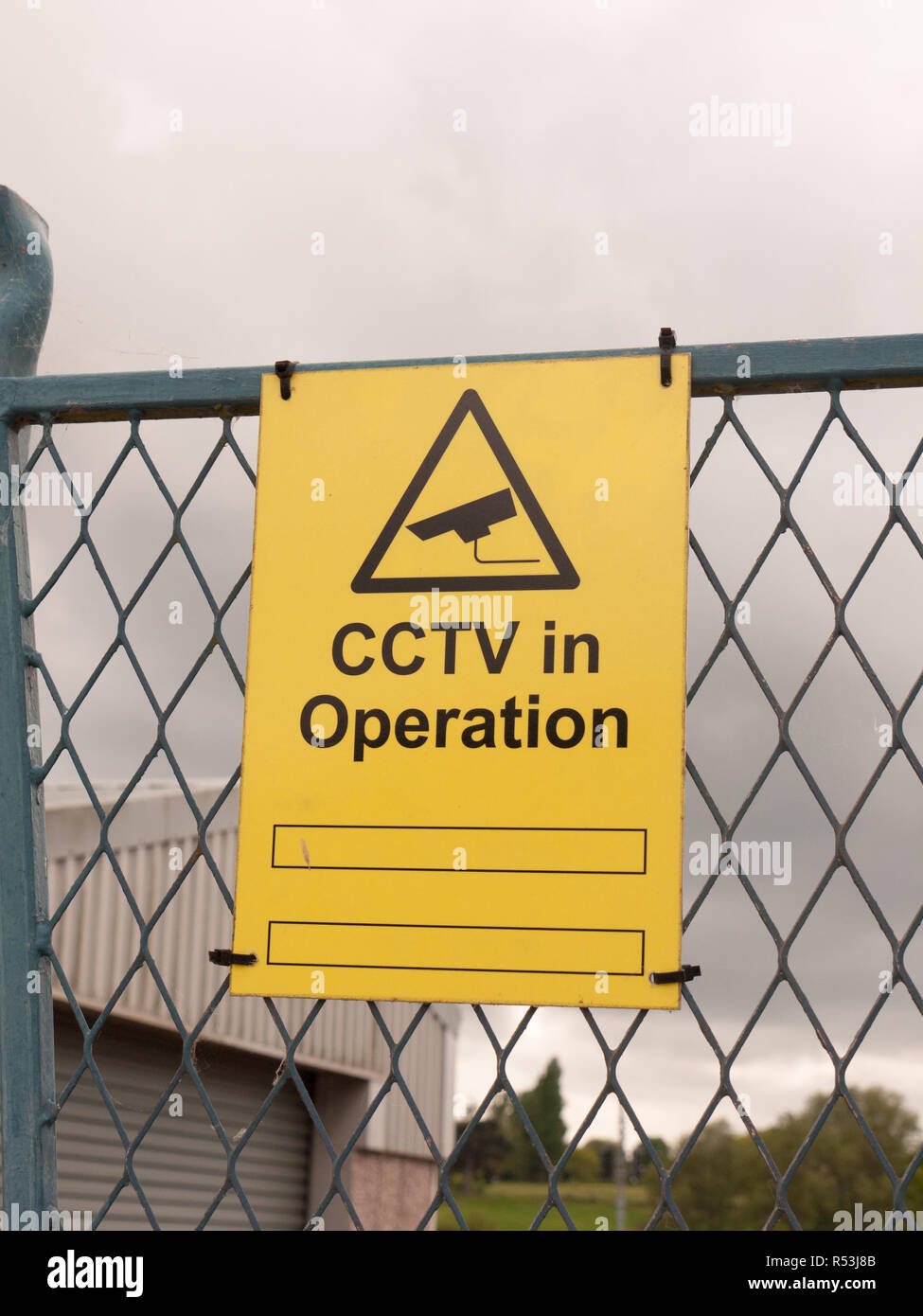 yellow sign on fence saying cctv in operation Stock Photo