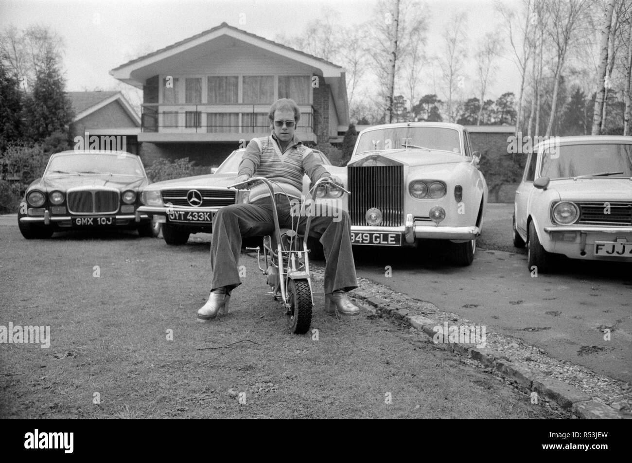 Elton John pictured at his home, sitting on a small motorbike in front of four of his cars. His cars include a Mercedes (2nd left) and a white Rolls Royce (3rd left)  Picture taken 4th April 1972 Stock Photo