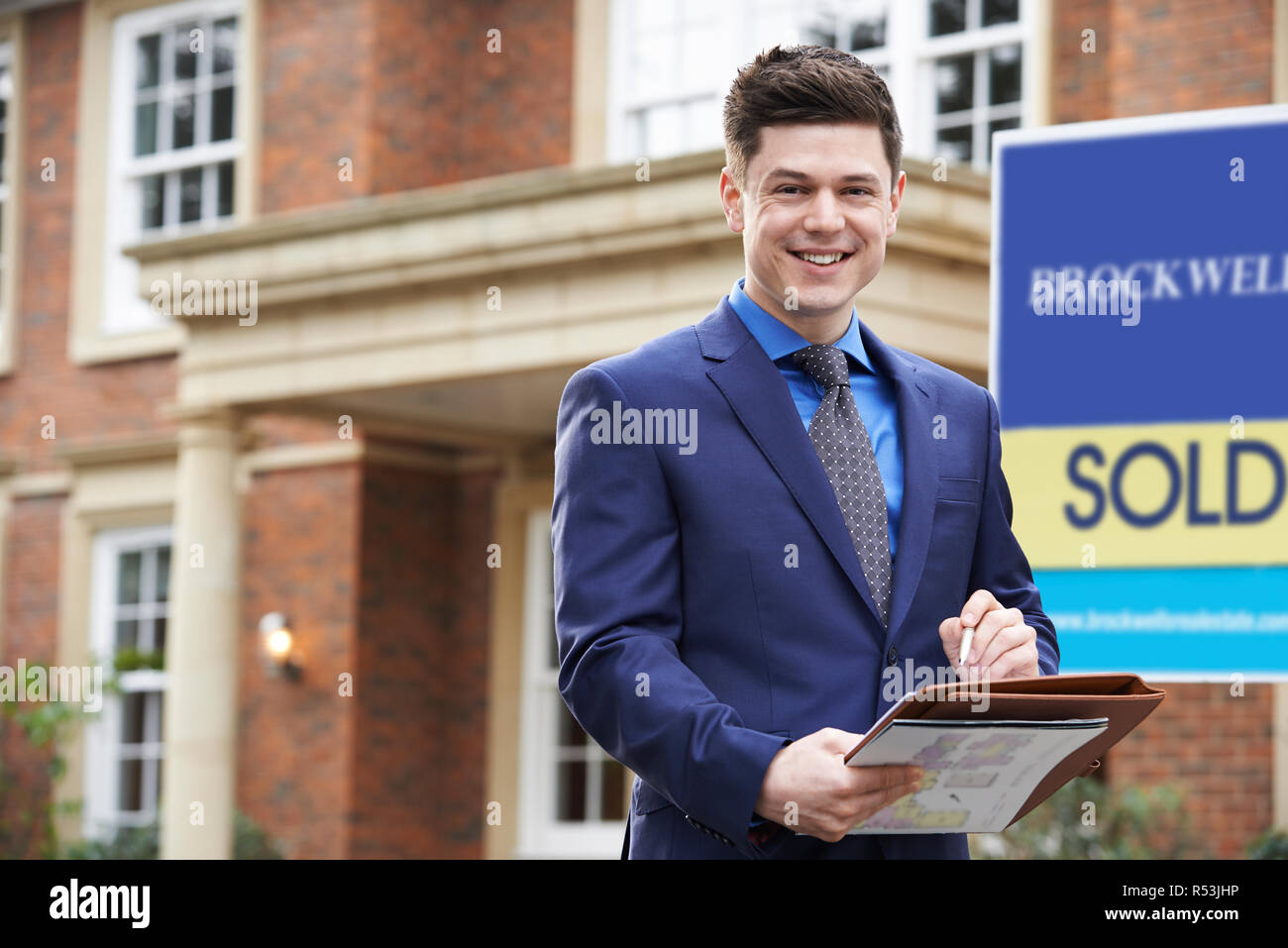 Portrait Of Male Realtor Standing Outside Residential Property With Sold Sign Stock Photo