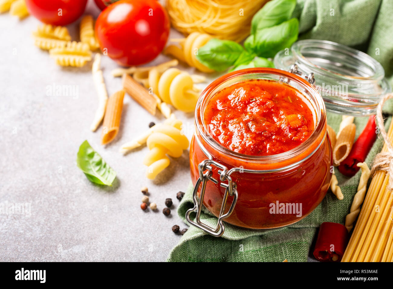 Glass jar with homemade classic spicy tomato pasta or pizza sauce with pine nuts and basil. Italian healthy food background. Copy space. Stock Photo