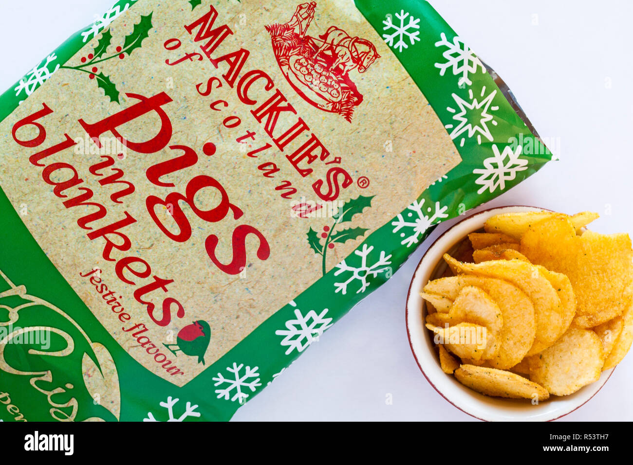 open packet of Mackie's of Scotland Pigs in Blankets festive flavour Potato Crisps with crisps in bowl set on white background - ready for Christmas Stock Photo