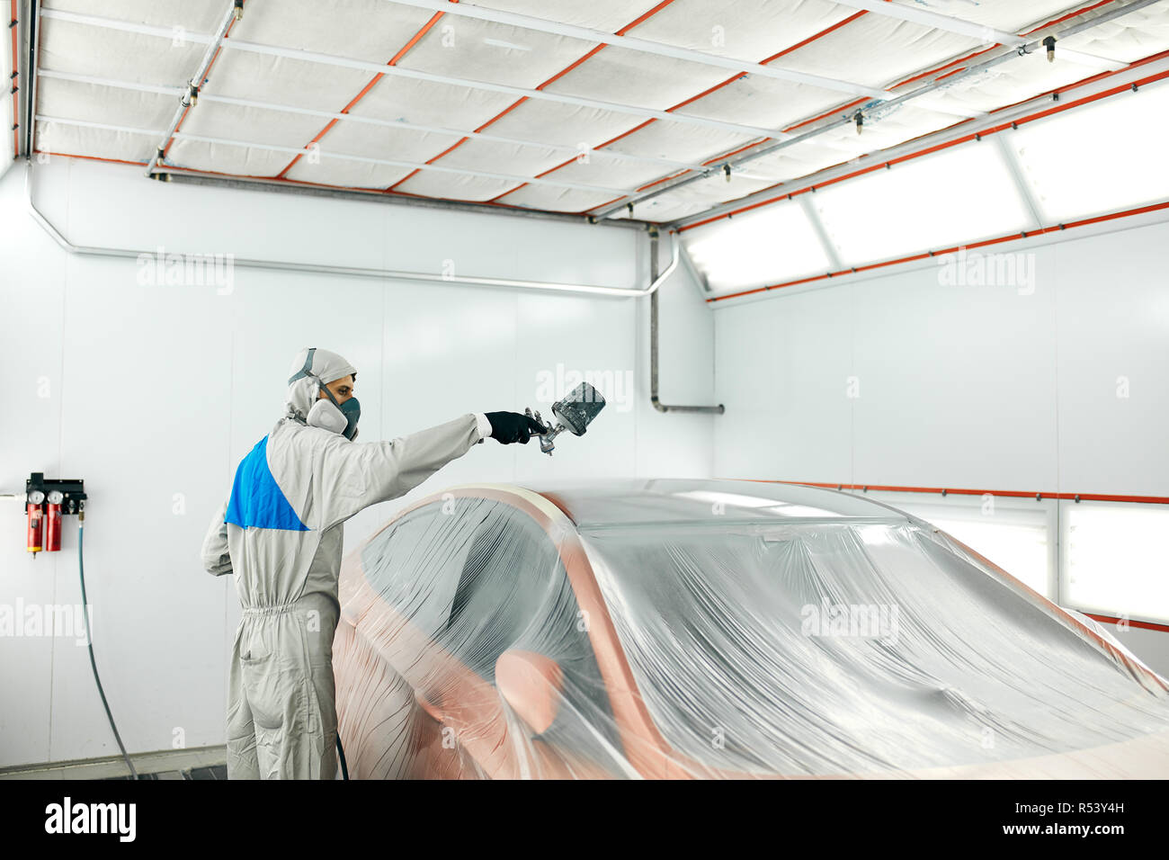 auto painter in protective workwear and respirator painting car body in